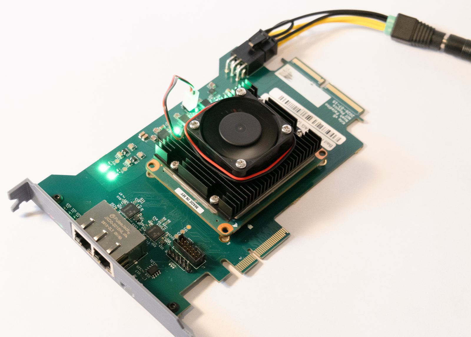 An assembled KrIO carrier lying flat and powered up: a Kria K26 module with heatsink and fan, two gigabit Ethernet jacks on a full-height bracket, the PCI Express card edge, and green power-rail LEDs lit.